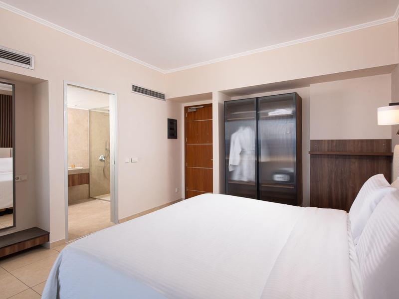 Helles Hotelzimmer mit Doppelbett, offenem Schrank und angrenzendem Bad.