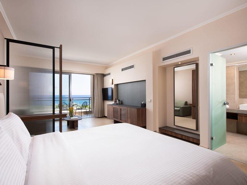 Modernes Hotelzimmer mit großem Bett, TV, Sitzecke und Blick auf das Meer.