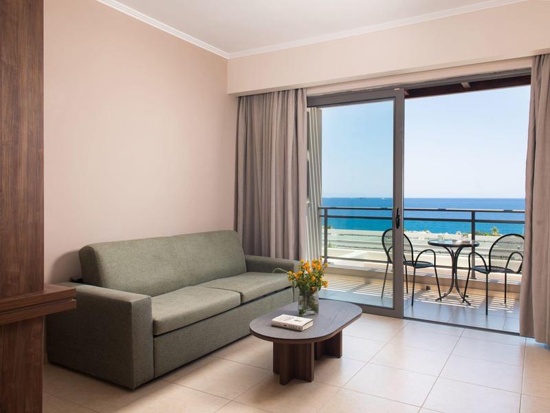 Modernes Hotelzimmer mit Sofa, Tisch und Balkon mit Meerblick und Sitzgelegenheit.