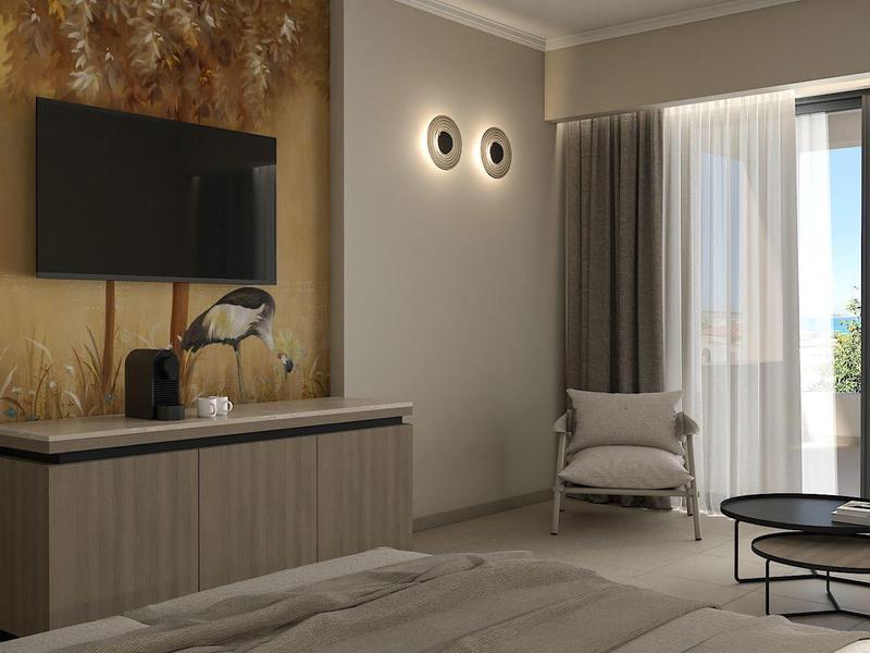 Helles Hotelzimmer mit großem Fenster, grauem Sessel und Wanddeko neben TV.