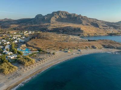 Línea costera con playa de arena, mar azul, hoteles y montañas al fondo con cielo despejado.