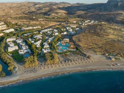 Vista aérea de un hotel con piscina junto a la playa y montañas cercanas.