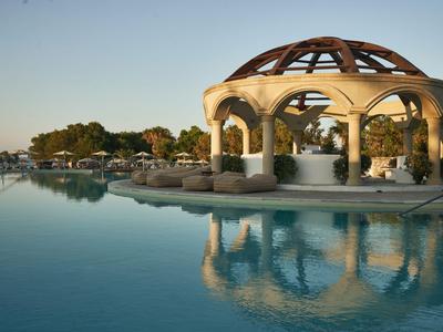 Un elegante padiglione con archi e cupola in legno accanto a una piscina tranquilla al tramonto.
