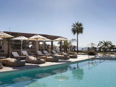Piscina moderna dell'hotel con lettini, ombrelloni e palme sotto un cielo limpido vicino al mare.