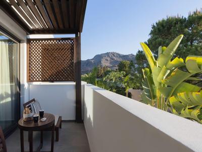 Balcone con tavolo e foto, vista su montagne e piante verdi sotto un cielo sereno.