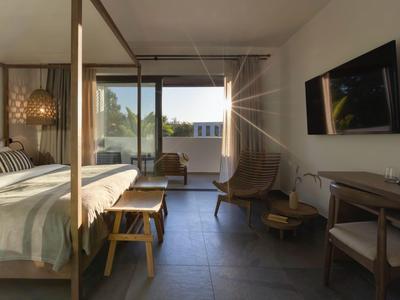 Camera d'hotel luminosa con letto grande, poltrone e balcone con vista esterna.