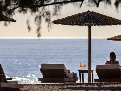 Spiaggia con lettini, ombrelloni di paglia e due bevande vicino al mare al tramonto.