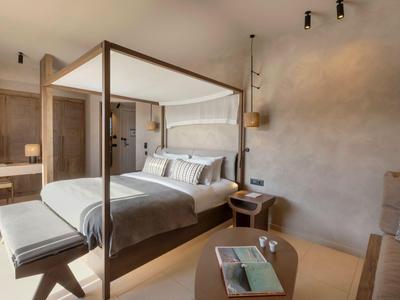 Camera d'hotel luminosa con letto a baldacchino, panca e piccolo tavolo.