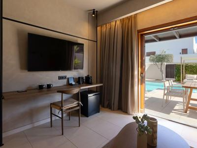 Camera d'hotel moderna con TV, scrivania e vista sulla terrazza con piscina.