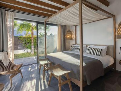 Camera d'hotel moderna con letto a baldacchino, mobili in legno e vista su giardino con palme.