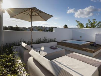 Area esterna moderna con posti a sedere, ombrellone e vasca idromassaggio sotto il sole.