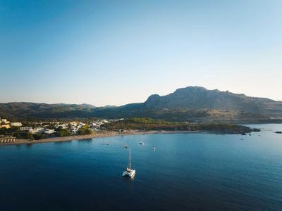 Barca a vela su acqua calma vicino a una costa con montagna e villaggio sotto un cielo sereno