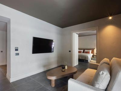 Camera d'hotel moderna con divano, tavolino e TV a parete in tonalità neutre.