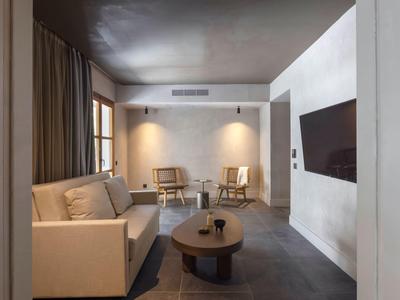 Area soggiorno moderna in hotel con divano, tavolino, due sedie e TV a parete