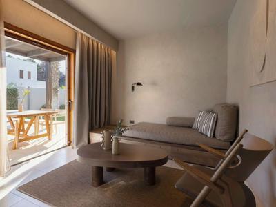 Soggiorno accogliente con divano, tappeto e accesso aperto a una terrazza con tavolo e sedie in legno.