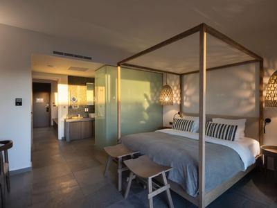 Camera d'hotel moderna con letto a baldacchino, panca e bagno aperto sotto luce calda.