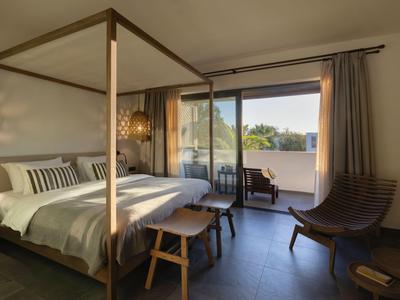 Camera d'hotel luminosa arredata con letto a baldacchino e balcone con vista.