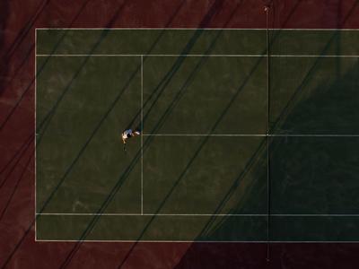 Un campo da tennis con un giocatore nella metà superiore sinistra, parzialmente all'ombra.