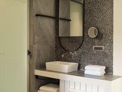 Baño moderno con espejo redondo, lavabo rectangular y azulejos grises en la pared.