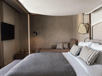 Habitación de hotel moderna con cama grande, cojines decorativos y un banco junto a la pared.