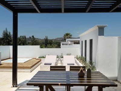 Terraza moderna de hotel con tumbonas, mesas de madera y vista a paisaje verde bajo cielo despejado.
