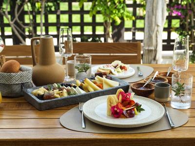 Una mesa de madera puesta con frutas frescas y bebidas, rodeada de sillas en el jardín.