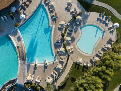 Vista aérea de una piscina de hotel con tumbonas y vegetación alrededor.