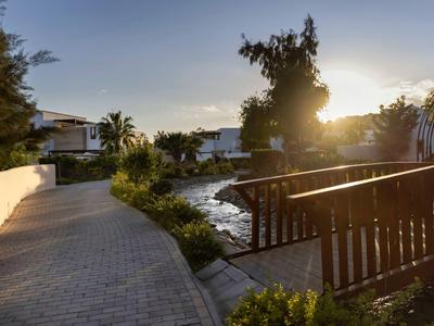 Atardecer en el jardín del hotel con camino, estanque y barandilla de madera en ambiente tranquilo.