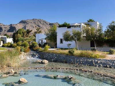 Casas blancas junto a un estanque con agua clara y montañas al fondo.