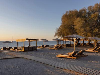 Playa de arena vacía con tumbonas de madera y sombrillas al atardecer junto al mar.