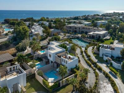 Vista aérea de un complejo turístico con villas modernas, piscinas y vista al mar en el horizonte.