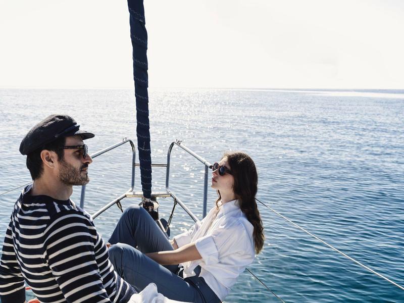 Dos personas sentadas relajadas en la proa de un velero mirando al mar.