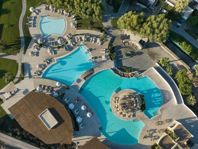 Vista aérea de un hotel con varias piscinas, rodeadas de tumbonas y áreas verdes.