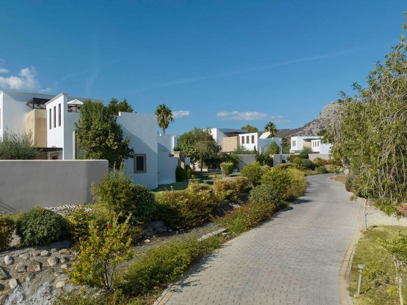 Complejo hotelero moderno con edificios blancos y un camino pavimentado bajo el sol.