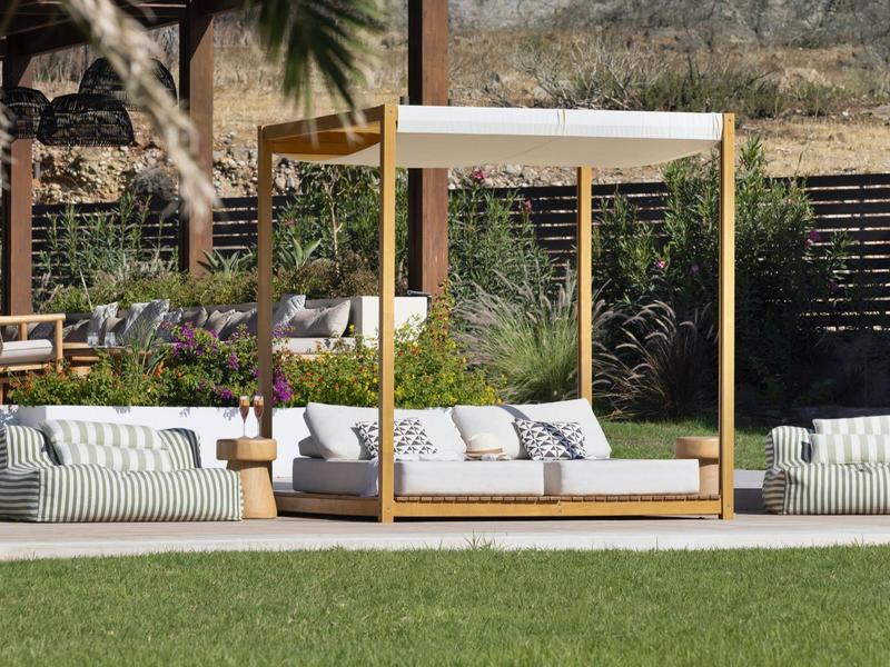 Sillón lounge moderno al aire libre con estructura de madera y cojines blancos frente a jardín.