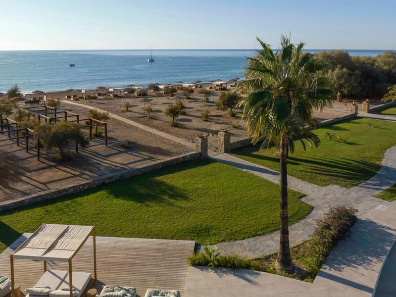 Vista de una playa con tumbonas, palmeras y área de césped bien cuidada bajo un cielo despejado.