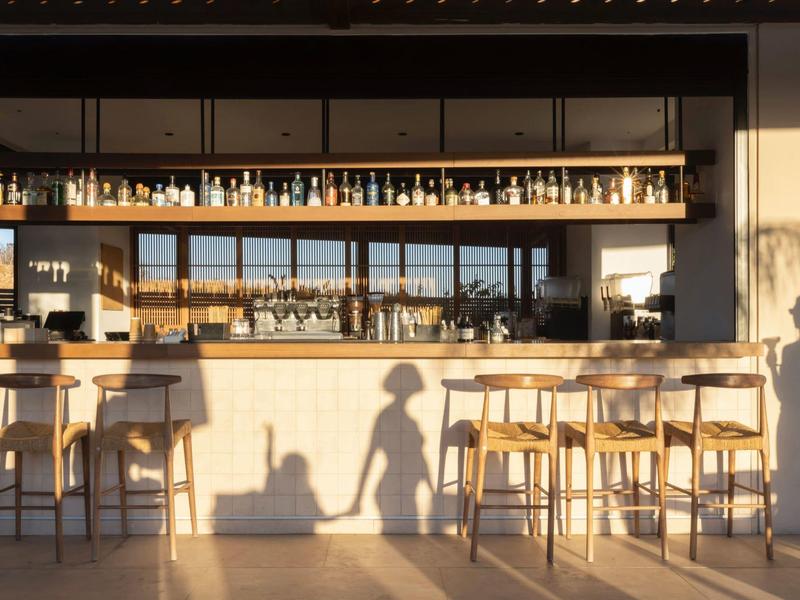 Bar moderno con sillas altas y botellas organizadas, iluminado por luz natural al atardecer