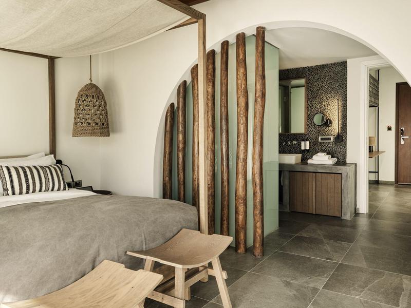 Habitación moderna de hotel con cama doble, muebles de madera y una elegante separación de espacio con barras de madera.