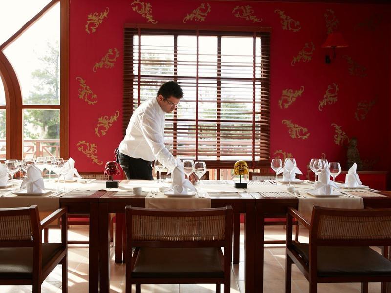 Un camarero arregla una mesa puesta en un restaurante decorado en rojo con ventanas de marco de madera.
