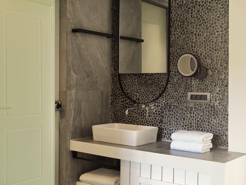 Baño moderno con espejo redondo, lavabo rectangular y azulejos grises en la pared.