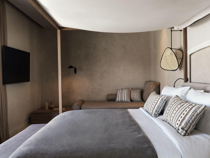 Habitación de hotel moderna con cama grande, cojines decorativos y un banco junto a la pared.