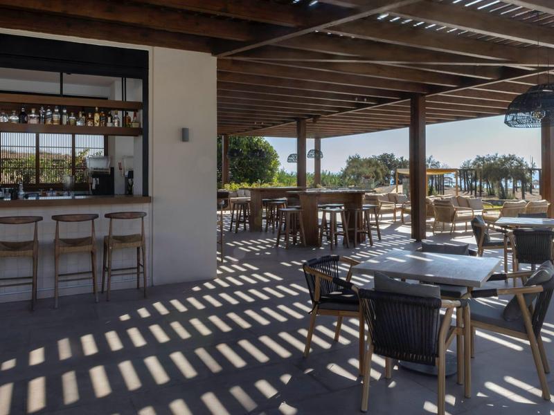 Terraza cubierta con mesas, sillas y barra con vista al agua y árboles.