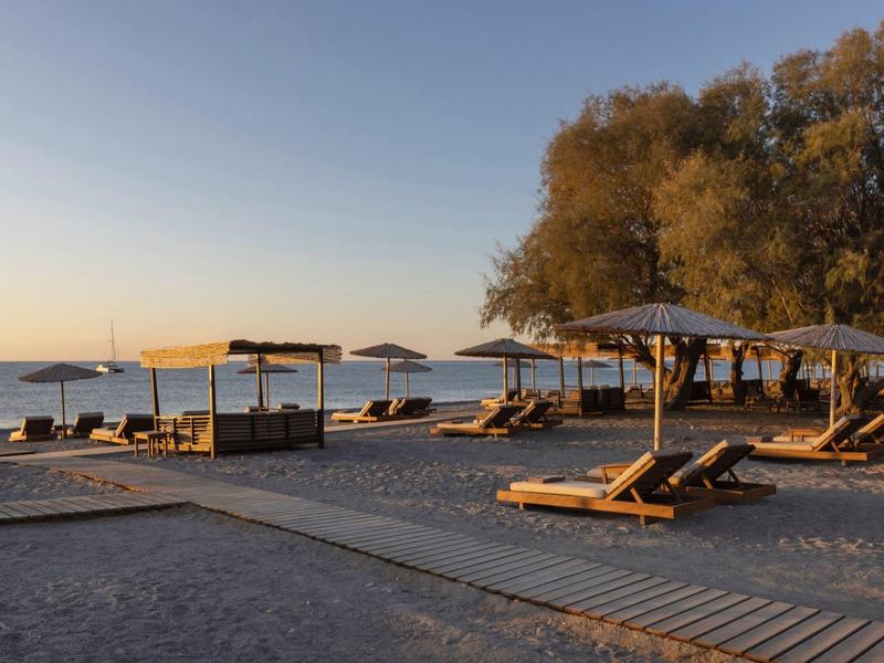 Playa de arena vacía con tumbonas de madera y sombrillas al atardecer junto al mar.