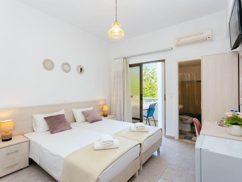 Modernes Schlafzimmer mit zwei Einzelbetten, weißen Wänden, Holzmöbeln und Zugang zu Balkon.