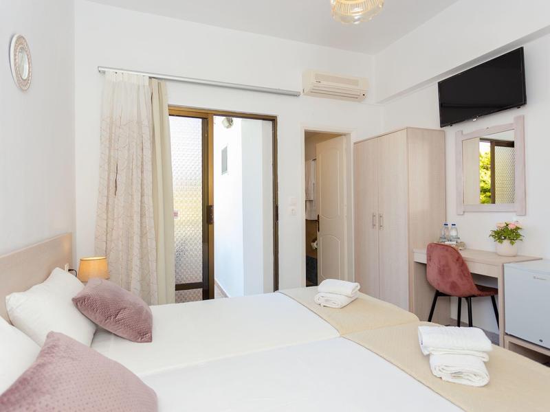 Hell eingerichtetes Schlafzimmer mit zwei Einzelbetten, Schreibtisch, TV und Balkonzugang.