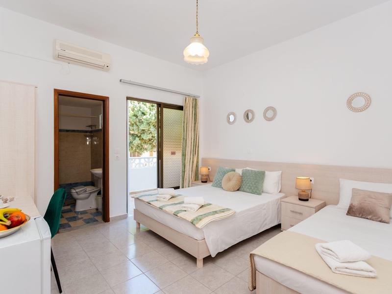 Hell eingerichtetes Schlafzimmer mit Doppelbett, Einzelbett, Schrank und Zugang zum Balkon.