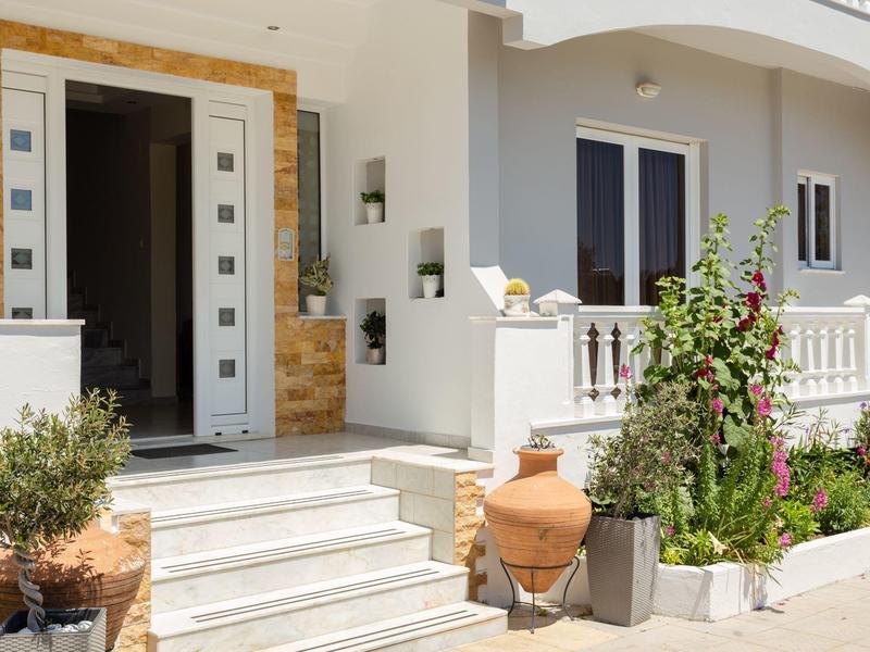 Moderner Hauseingang mit weißen Treppen, großen Töpfen und blühenden Pflanzen am Geländer.