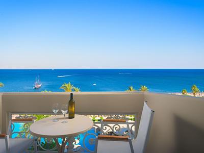 Balkon mit Tisch, Stühlen und Blick auf das blaue Meer bei klarem Himmel.