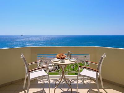 Balkon mit zwei Stühlen und einem Tisch mit Frühstück, Meerblick bei klarem Himmel.