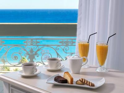 Frühstück mit Kaffee, Kuchen und Saft auf Tisch vor Balkon mit Meerblick.